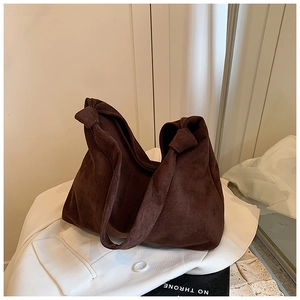Detailed view of dark brown suede tote bag featuring a large knot strap design on a white blazer