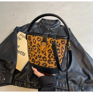 Borsa a secchiello leopardata con manico in pelle nera su una giacca di pelle