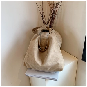 Close-up of beige suede tote bag with stylish knot handle detail on display stand
