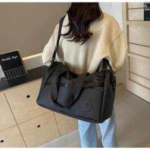 Grande borsa da viaggio nera indossata da un modello con tracolla e dettaglio logo
