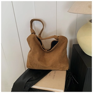 Detail of a brown suede tote bag featuring a decorative knotted strap and magnetic closure
