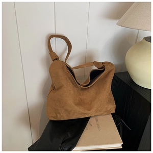 Detail of a brown suede hobo bag with a distinctive knotted strap on a stack of books