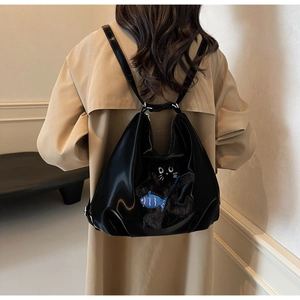 Détail d'un sac à dos en cuir noir orné d'un chat en peluche et d'un pendentif poisson