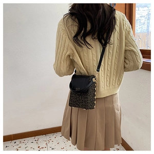 Detail of a leopard print crossbody bucket bag with black flap and gold hardware accents