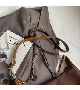 Detail of dark brown leather crescent bag with metal chain and adjustable long shoulder strap