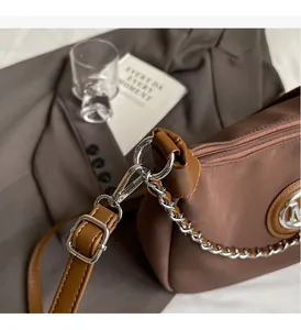 Detail of silver chain and M logo plate on brown nylon tote bag with zipper