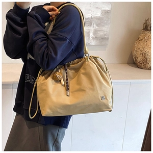Detail of khaki drawstring bucket bag featuring a metal flower logo and spherical charm