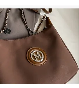 Close-up of coffee brown suede dumpling bag featuring a silver metal M logo and chain strap