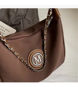 Detail of brown nylon dumpling bag with M-logo metallic plaque and chain strap