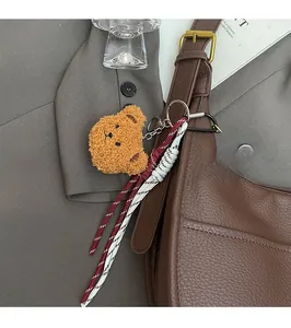 Detail of a brown plush bear bag charm with woven rope and metal hook on leather