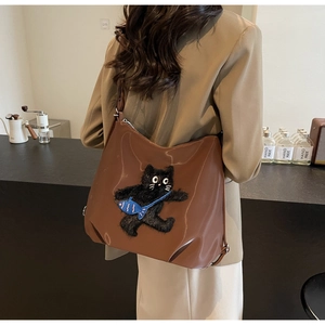 Détail d'un sac cabas marron brillant avec broderie de chat noir porté à l'épaule