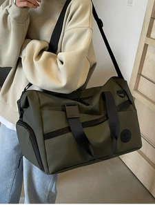 Borsa da viaggio verde oliva con tracolla indossata da un modello in un ambiente moderno