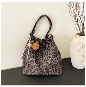 Detail view of leopard print bucket bag with drawstring closure and plush bear charm