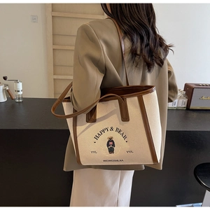 Detailed shoulder view of large canvas tote bag with bear embroidery and brown leather trim