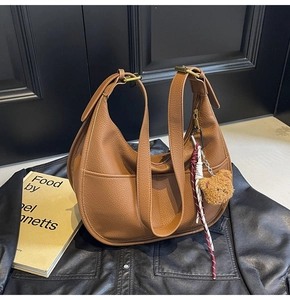 Detail of brown lychee leather handbag with cute plush bear charm and woven rope accent