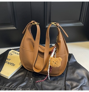 Detail of brown crescent bag featuring litchi grain texture and a cute plush bear charm
