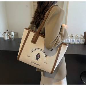 Detail of canvas tote bag featuring embroidered bear and brown faux leather trim details