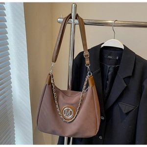 Detail of a brown tote bag featuring a silver metal M logo and elegant chain strap