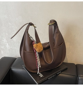 Detailed shot of brown lychee leather dumpling bag with bear pendant and woven charm