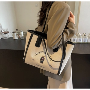 Lifestyle shot of large beige canvas tote bag with bear embroidery and black leather trim