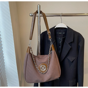 Close-up of taupe hobo bag with silver M logo and chain on a metal display stand