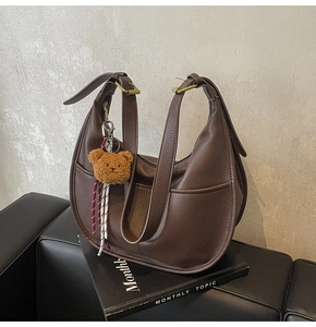 Detail of dark brown pebble leather hobo bag with teddy bear charm and brass buckle