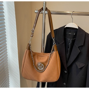 Detail of caramel brown half-moon shoulder bag featuring silver M logo and chain