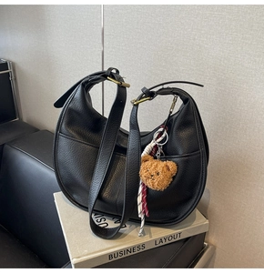 Detail of black lychee leather dumpling bag with brass hardware and cute bear charm