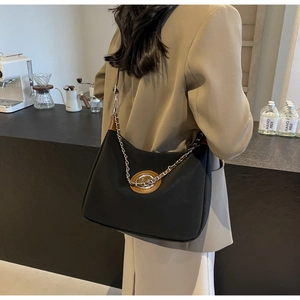 Detail of black croissant bag with metallic chain strap and brown leather logo patch