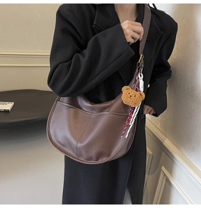 Detail of dark brown lychee textured crescent bag with cute bear charm on shoulder