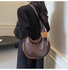 Detail of dark brown leather hobo bag with teddy bear charm on model in black suit
