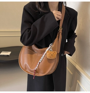 Brown lychee leather crescent bag with plush bear charm and woven tassel detail