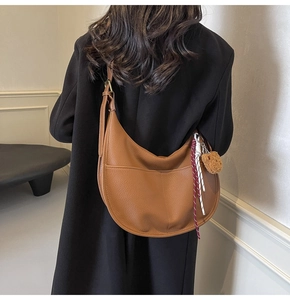 Detail view of brown leather crescent bag with teddy charm on a black wool coat
