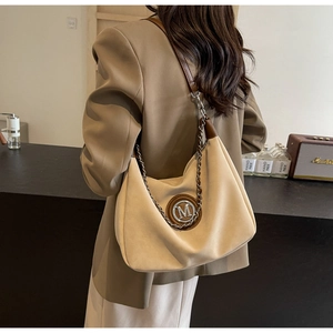 Close-up of beige canvas shoulder bag with brown leather trim and metallic M logo