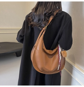 Close-up of brown lychee leather crescent bag with decorative plush ball and charm
