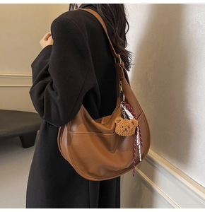 Model wearing a brown leather hobo bag with a plush bear charm and woven detail