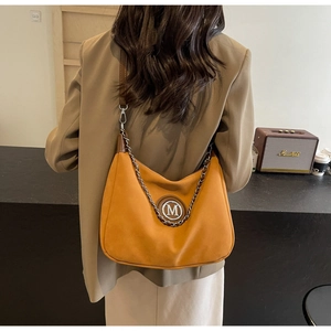 Close-up of mustard yellow suede tote bag with silver chain and metal M logo detail