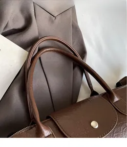 Detail of dark brown leather tote bag showing handle texture and silver metallic buckle
