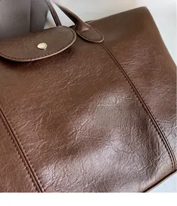 Detailed close-up of brown textured leather tote bag featuring a round metal snap button