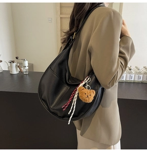 Close-up of black leather dumpling bag with cute bear charm and woven rope detail