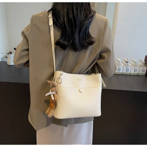 Detail of off-white lychee leather bucket bag with a cute brown rabbit plush charm