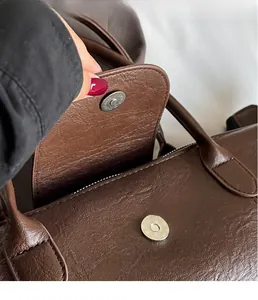 Detail view of the vintage brown leather tote bag showing the metallic magnetic closure