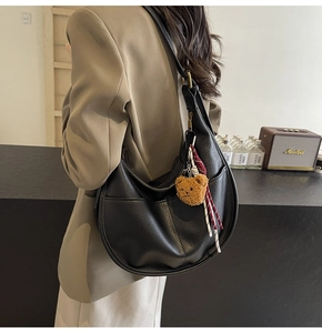 Detail of black pebbled faux leather dumpling bag with brown plush bear accessory