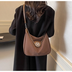 Close-up of brown crescent bag featuring silver M-logo and chain detail on black coat