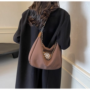 Detail view of brown hobo bag with silver chain strap and M logo on black wool coat