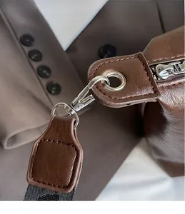 Macro shot of silver metal hooks and woven strap detail on dark brown leather tote bag