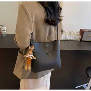 Detail of black lychee grain bucket bag with golden logo and cute rabbit charm accent