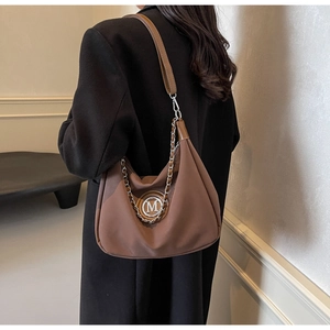 Detail of brown hobo bag featuring silver M-logo charm and metallic chain strap