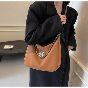 Detail of caramel brown leather saddle bag with silver M logo and chain on a model