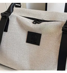 Detail of canvas tote bag with black leather trim and embossed brand logo on front